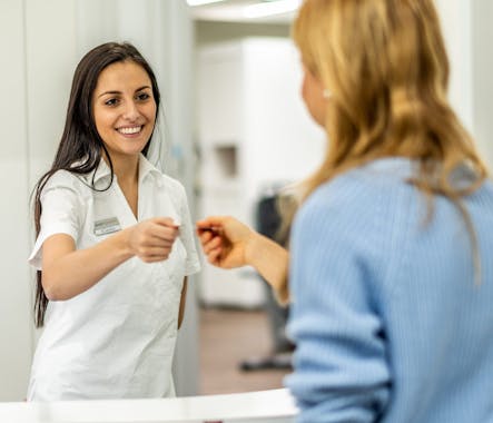 Praxisassistentin überreicht einer Patientin die Terminkarte